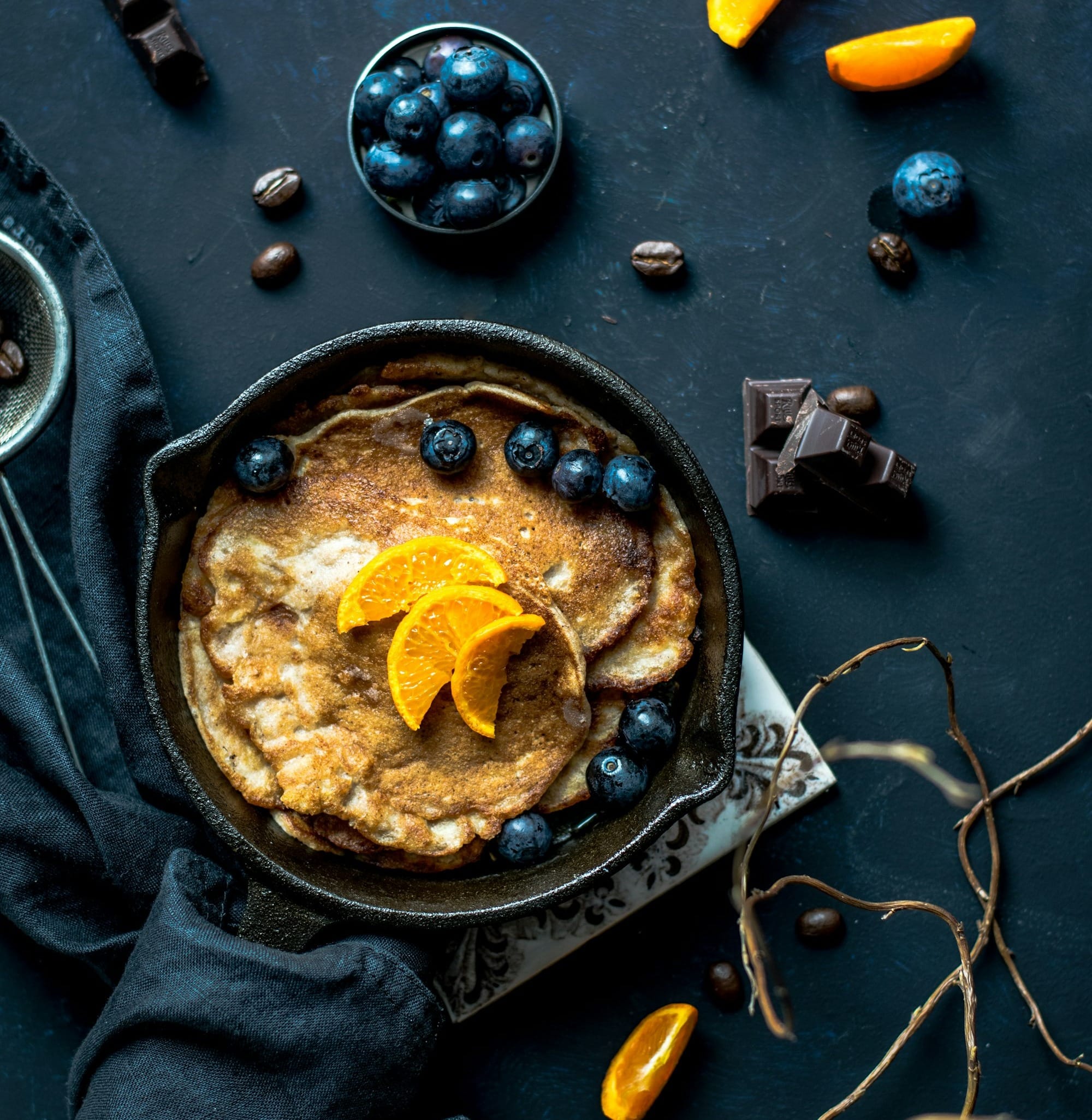 pancake with orange and blueberries beside scattered chocolate and coffee beans